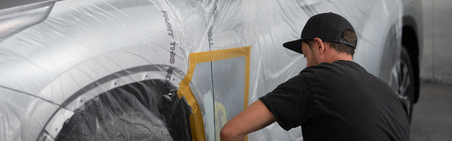 L-M Body Shop technician masking a silver SUV for paint in the Kirkland shop